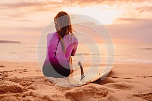 Surfer girl with surfboard on a beach at sunset