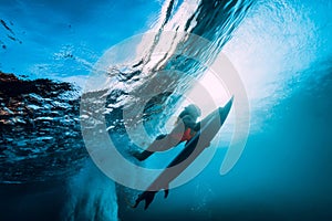 Surfer girl with surfboard dive underwater with fun under big ocean wave.