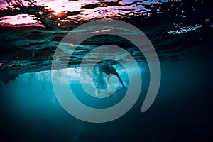 Surfer girl with surfboard dive underwater with ocean wave.