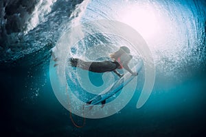 Surfer girl with surfboard dive underwater with under barrel ocean wave.