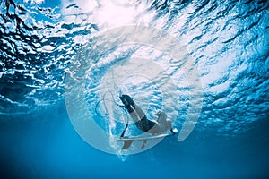 Surfer girl with surfboard dive underwater under ocean wave