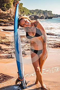Surfer girl with surfboard near the ocean. Young sexy woman wearing black bikini. Happy surfer girl at the beach. Bali, Indonesia