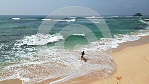 Surfer girl with surfboard walking on the beach towards ocean tide view from drone. Aerial shot of female surfer and