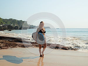 Surfer girl with surfboard walking at the beach. Young sexy woman wearing black bikini. Surfer girl preparing to surf. Bali,