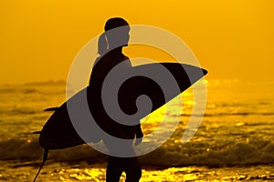 Surfer girl surfing looking at ocean beach sunset. Silhouette w