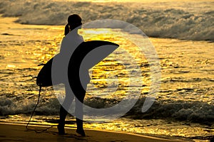 Surfer girl surfing looking at ocean beach sunset. Silhouette w