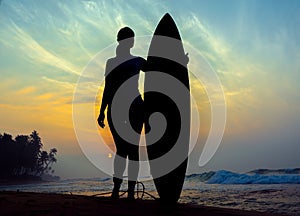 Surfer girl surfing looking at ocean beach sunset. Silhouette w