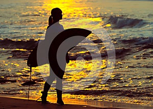 Surfer girl surfing looking at ocean beach sunset. Silhouette w