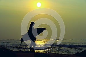 Surfer girl surfing looking at ocean beach sunset. Silhouette w