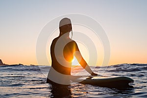 Surfer girl waiting for a wave in the water at sunset
