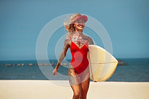 Surfer girl wearing in red visor and swimwear, running with board on the sandy beach