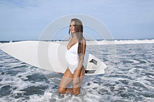 Surfer girl in a white swimsuit goes to the blue ocean, with a white surfboard