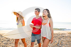 Surfer girls with teen boy walking on beach shore