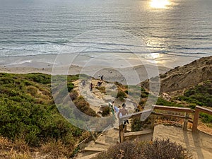 Surfer with his surf board going down the cliff to the beach during sunset