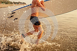 A surfer man with his surfboard going to meet the sea waves evening sunset on the beach.male freelancer surfing on