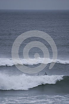 A surfer paddles on his surfboard towards a breaking approaching wave on a beach in Portugal