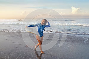 Surfer Portrait. Surfing Girl Carrying Surfboard. Smiling Brunette In Blue Wetsuit Walking On Ocean Beach At Sunset.