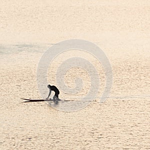 A surfer pushing his surfboard at sunset