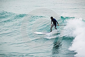 Surfer on stand up paddle board on blue wave. Winter surfing in ocean