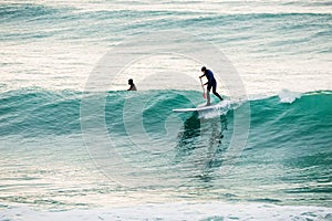 Surfer on stand up paddle board on blue wave. Winter surfing in sea