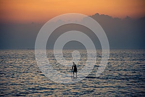 Surfer rowing his board against cloudy sunset