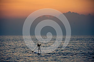 Surfer rowing his board against cloudy sunset