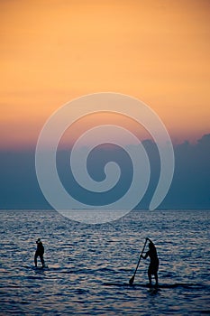 Surfer rowing his board against cloudy sunset in background