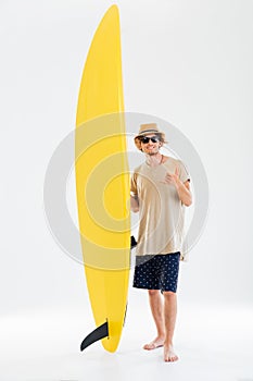 Surfer showing shaka or hang loose sign and holding surfboard