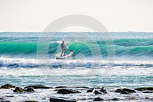 Surfer on stand up paddle board on blue wave. SUP surfing in ocean