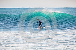 Surfer on stand up paddle board on blue wave. Winter surfing in ocean