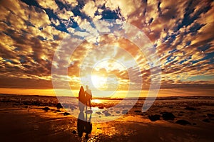 Surfer standing with his surfboard on the beach at sunset over the ocean