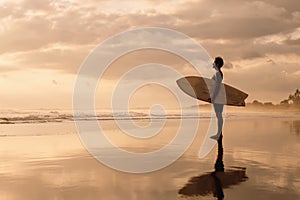 Surfer stands on sunset ocean beach