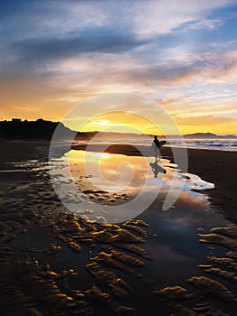 Surfer at sunset with reflection on puddle