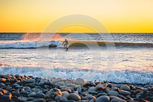 Surfer at sunset or sunrise. Winter cold surfing in wetsuit