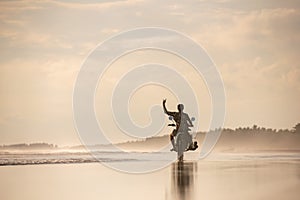 Surfer with surfboard on motorbike at sunset beach