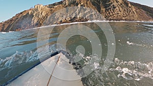 Surfer on surfboard riding on a crashing wave. First-person view of surfing in ocean at sunrise