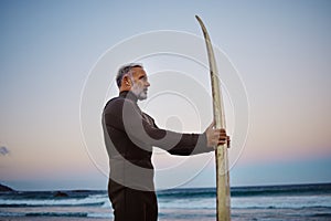 Surfer, surfboard and senior man at the beach during sunset after surfing on the waves in the sea water. Elderly male on