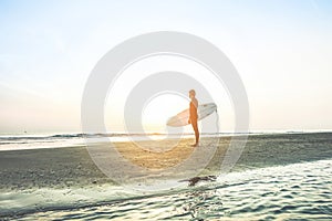 Surfer waiting for high waves at sunrise - Man standing on the beach with his surfboard outdoor - Extreme sport concept - Focus on