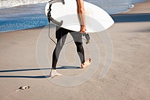 Surfer walking on the beach carrying his surfboard