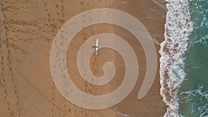 Surfer walking beach sand carrying surfboard top view. Beautiful ocean foaming