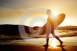 Surfer walking on beach with surfboard during sunset