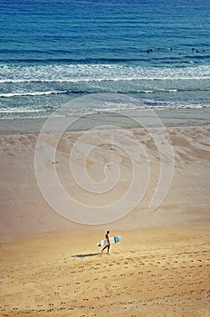 Surfer walking on the sandy beach, ocean in the background.