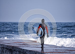 Surfer walks into ocean wearing a wetsuit in winter