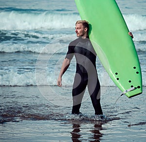 Surfer wearing wetsuit standing on the beach with a surfboard