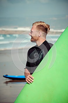 Surfer wearing wetsuit standing on the beach with a surfing board