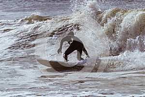 Surfer in a wetsuit carving through ocean waves. Winter cold weather surfing  - Long Beach, NY