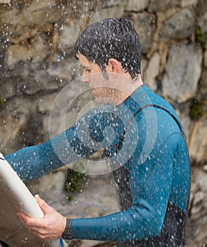 Surfer in wetsuit cleaning board in the shower