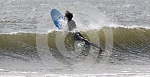 Surfer in a wetsuit splashing through a wave swimming out to go surfing