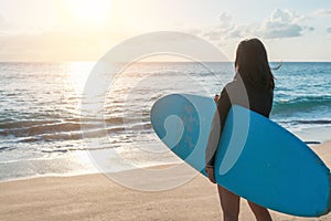 Surfer woman carrying their surfboards on sunset beach with sun light