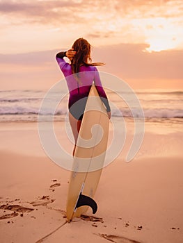 Surfer woman posing with surfboard on the beach at sunset